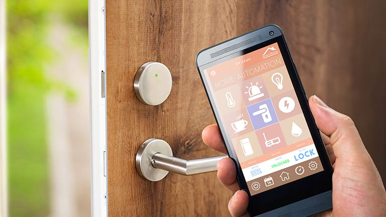 Person holding smartphone running home automation app, by door.