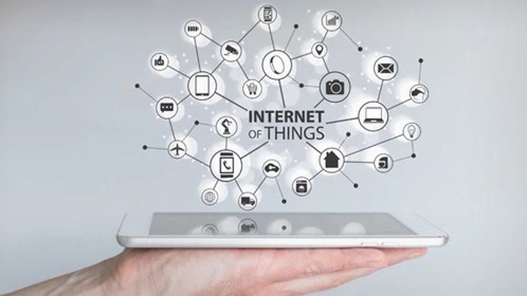 A hand holding a tablet with an illustration of the Internet of Things hovering above it